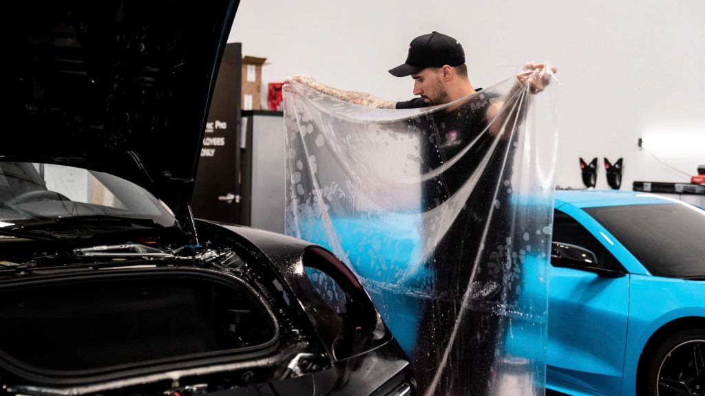 employee hold spread out clear film over a black car